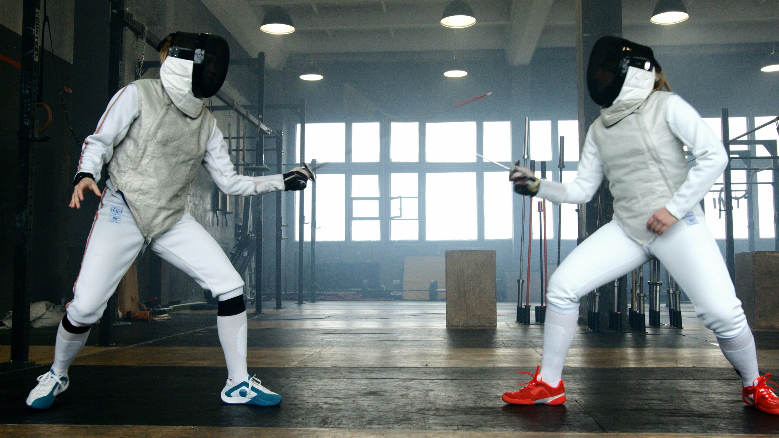 Two fencers compete in an intense epee match within a modern indoor gym, showcasing skill and equipment.