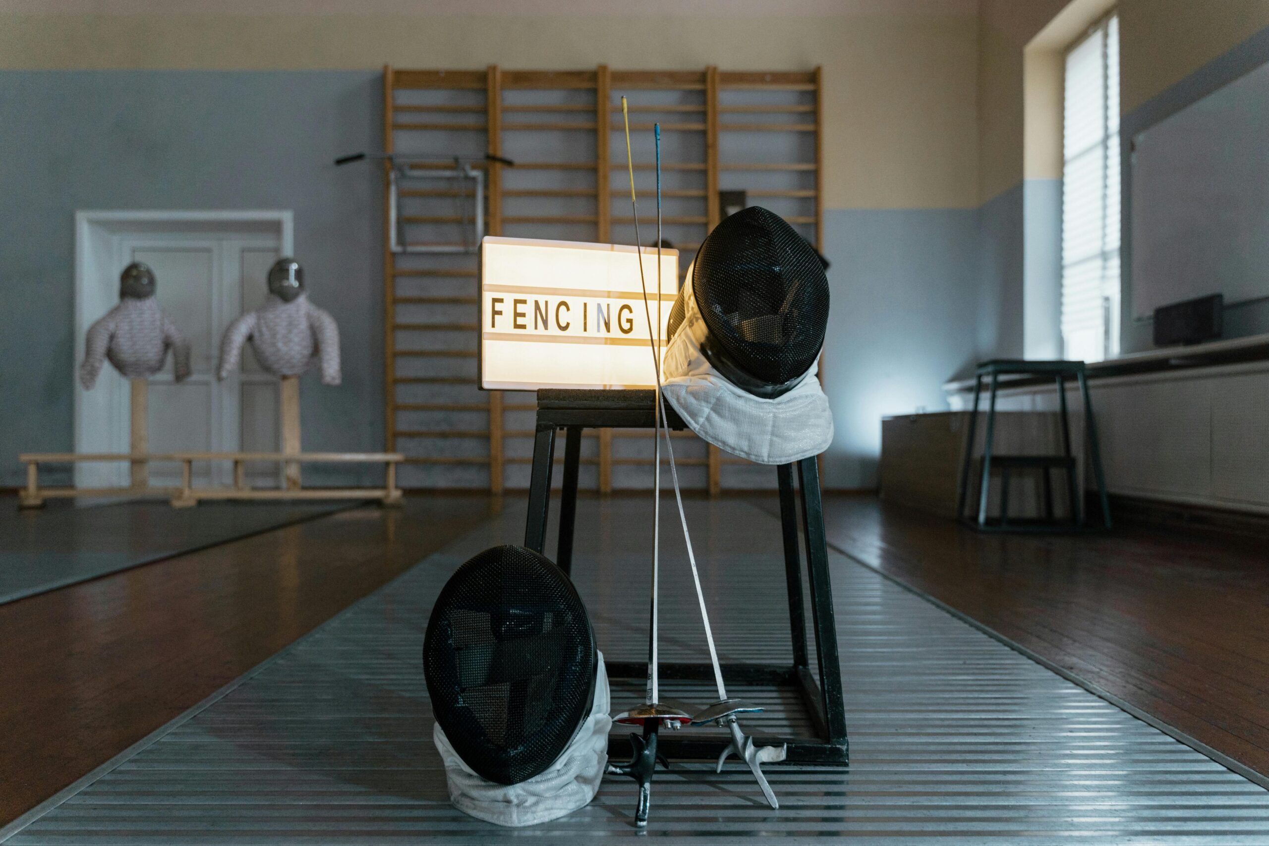 Fencing gear including masks and swords displayed in a training room.