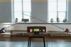 Two fencers engaged in a duel with the scoreboard showing 8:4 indoors.