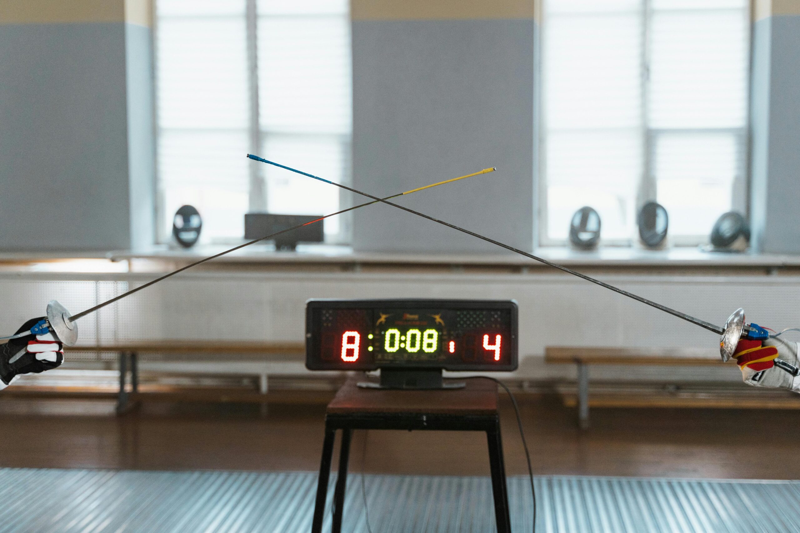 Two fencers engaged in a duel with the scoreboard showing 8:4 indoors.